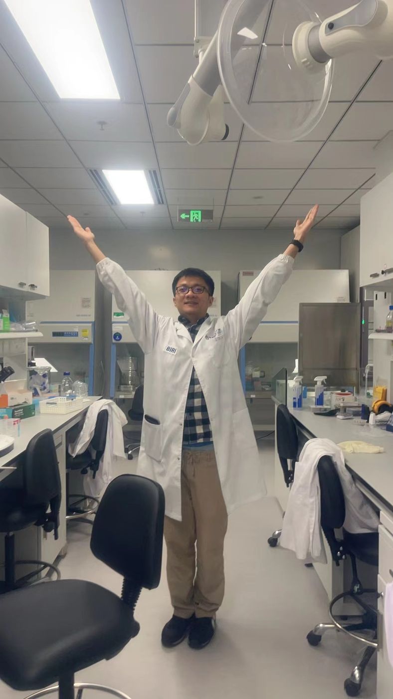 Lab member in a lab coat with arms raised between the benches