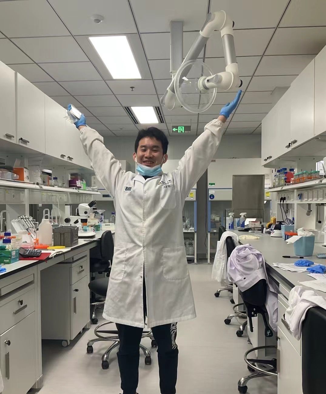 Lab member in a lab coat with arms raised in the lab aisle